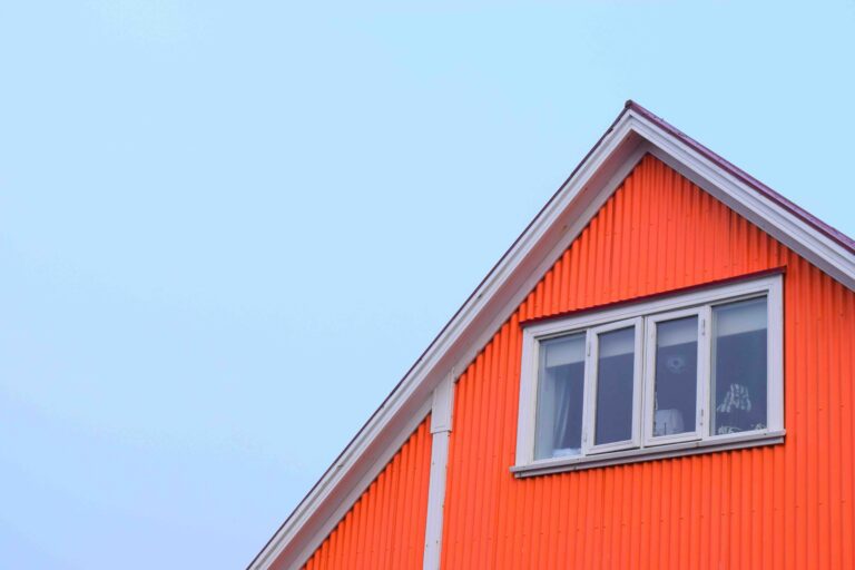 Side of an orange-clad wooden home with a white-framed window and peaked roof.