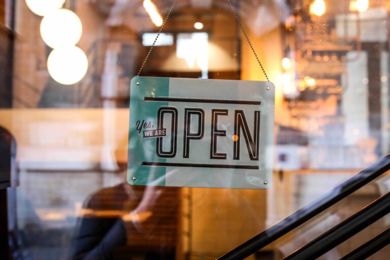 Yes We Are OPEN sign hanging in a storefront window with warm bokeh background.