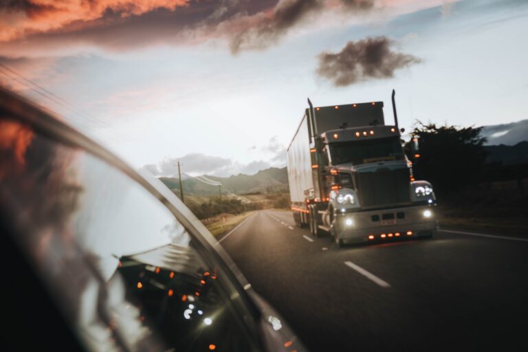 Semi-trailer truck driving on a highway at sunset seen from a passing car window.